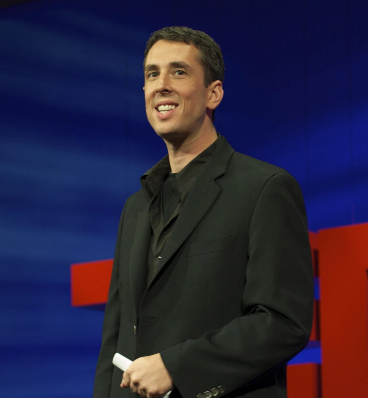 Marc Hodosh speaking onstage at TEDMED, wearing a black suit against a blue backdrop.